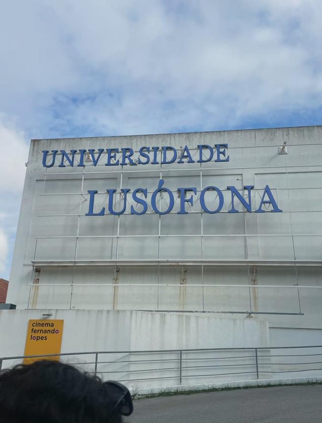 A gray, concrete building has a sign that says "Universidade Lusofona" in blue letters.