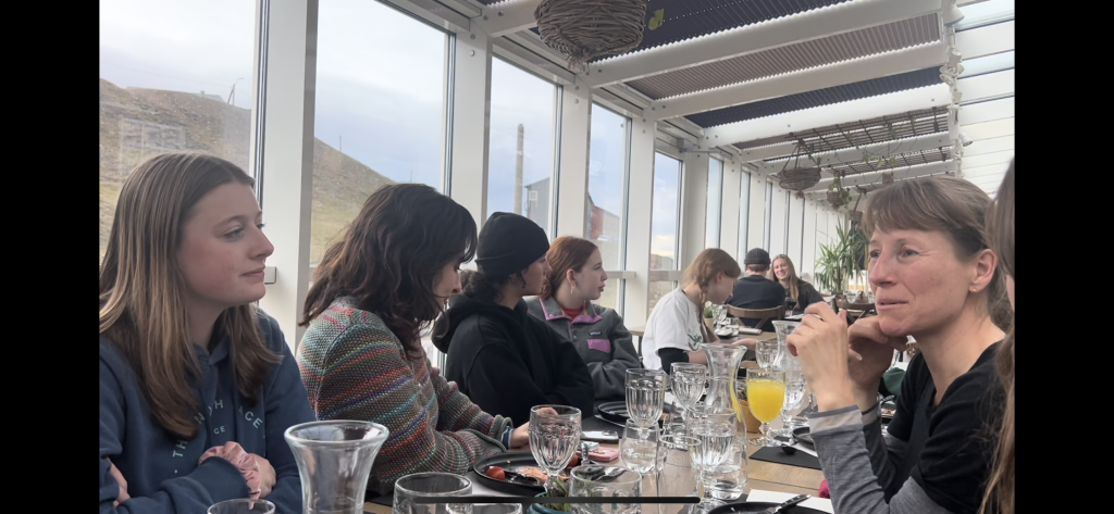 A long table lined with people in a room with a lot of windows.