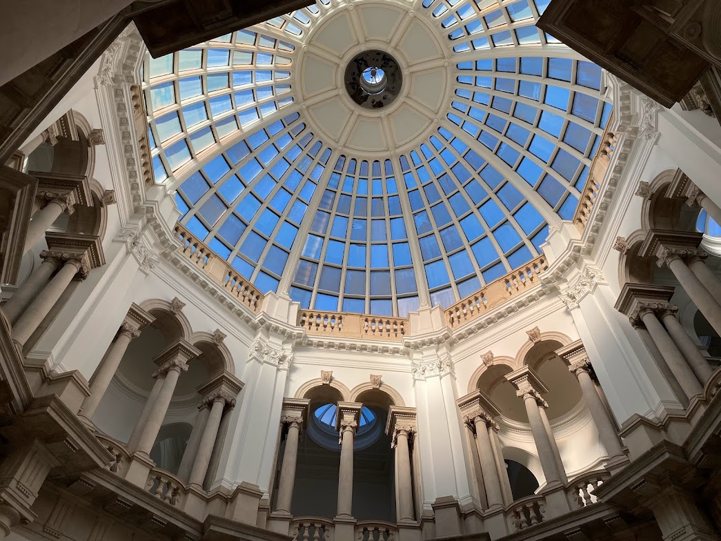 Interior view of a domed skylight spanning ornate white pillars.