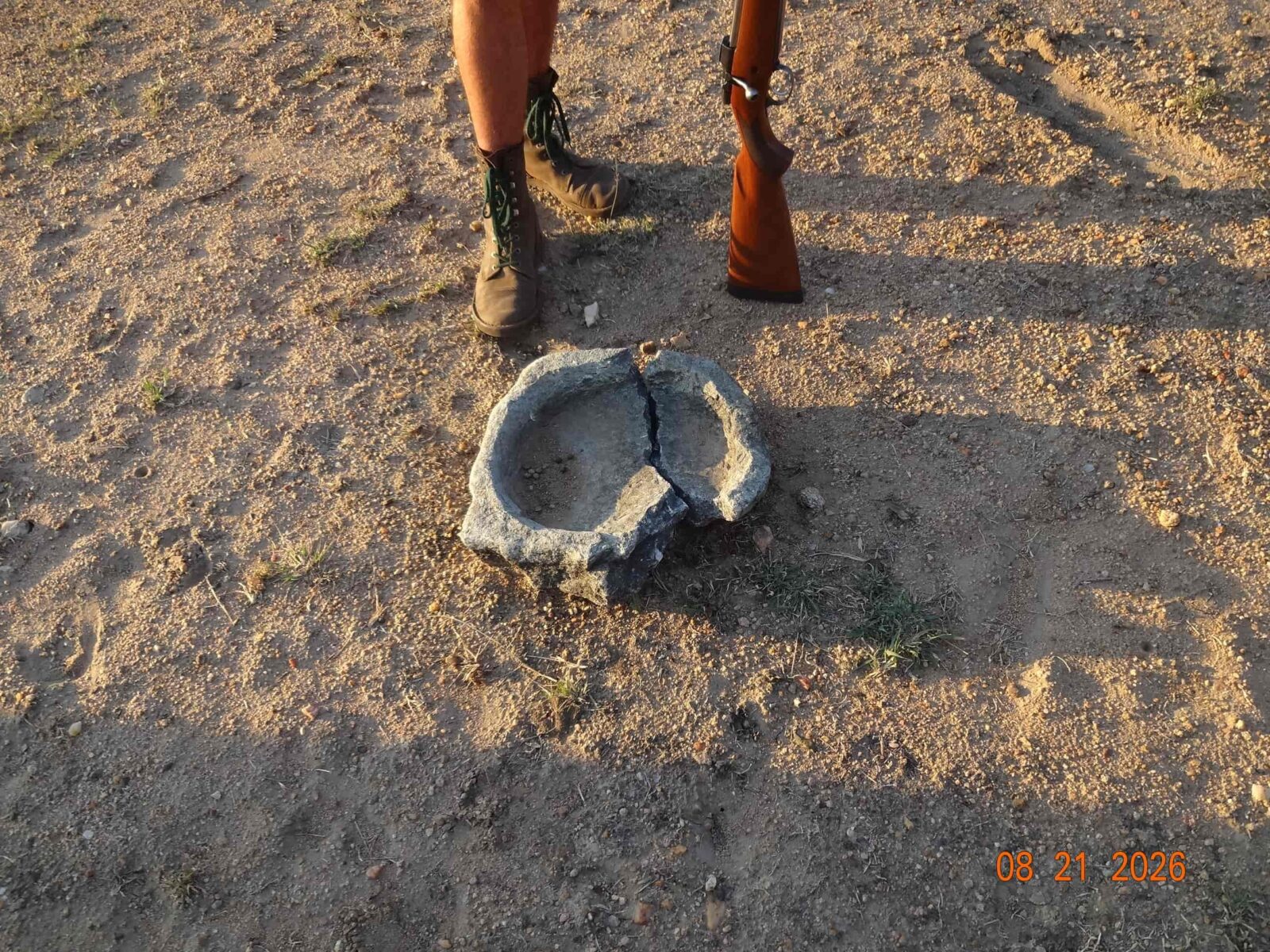A large cracked bowl, resting on a sandy surface, with a person standing over it.