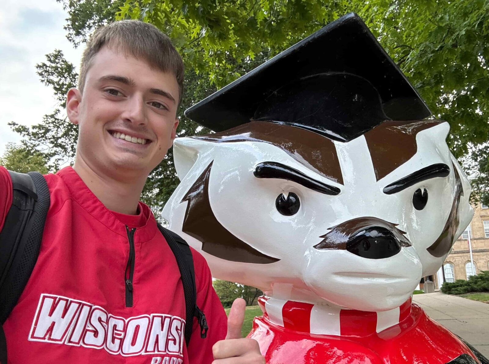 A man in a red Wisconsin Badgers jacket gives a thumbs up to the calendar standing next to a statue of Bucky Badger.