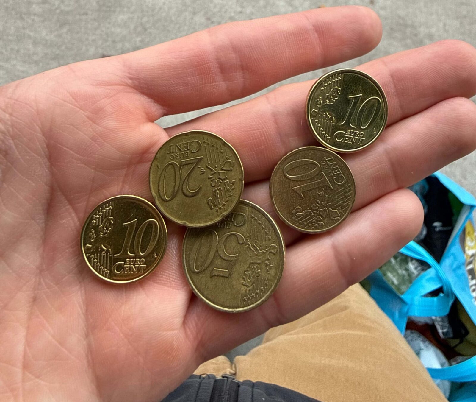 A hand holding five different Euro coins of varying amounts.