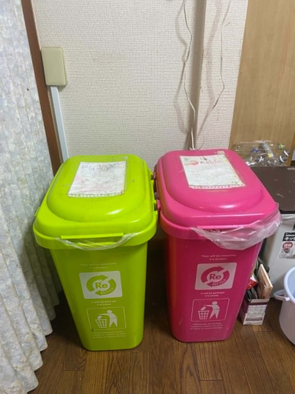 Two trash bins, one bright green and one bright pink, in the corner of a room.