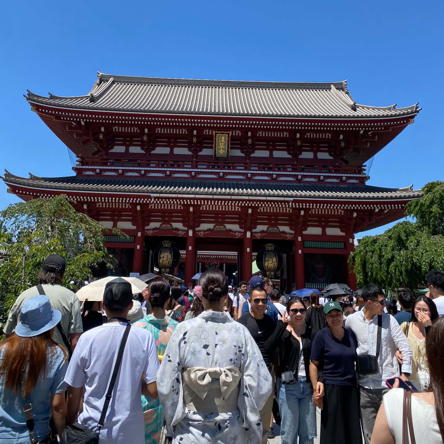 Many people standing and walking in front of the large, red Sensoji Temple.