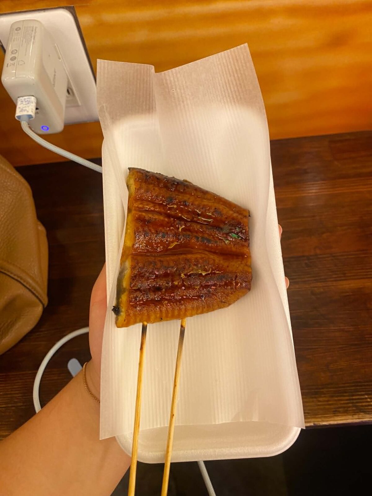 Cooked eel, held over a small tray on two wooden sticks.
