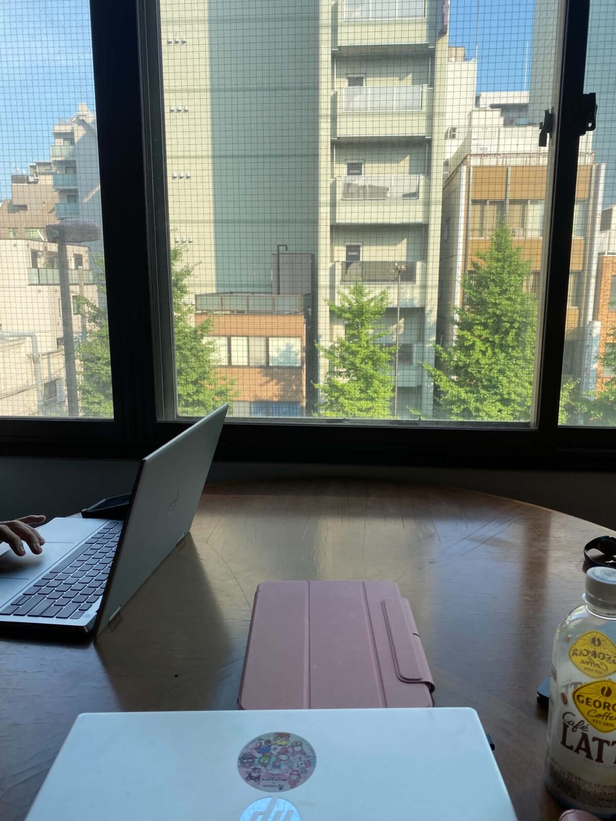 Two computers and and iPad on a table, facing a window with views or a large building.