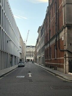 A London Street with a white building on the left and an brown building on the right. There is one white car parked on the left side of the street.