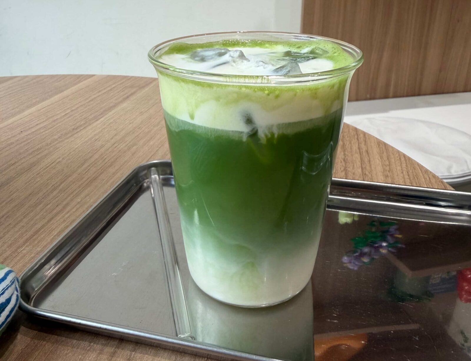 A plastic cup with a green and white drink on a tray with a plastic straw.