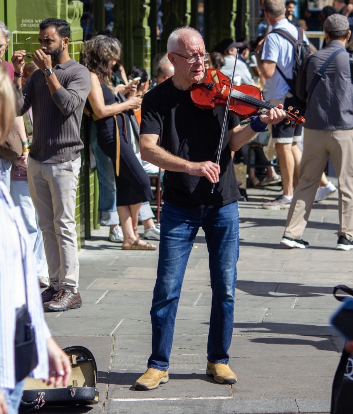 An elderly man playing a violin on a crowded sidewalk