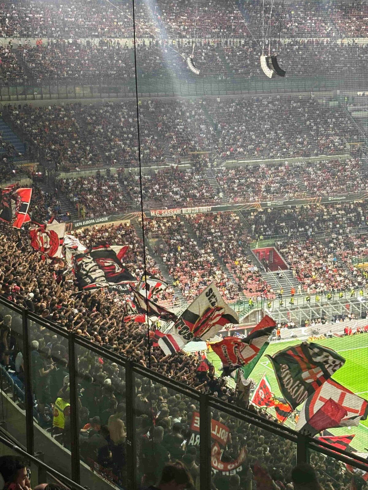 A packed soccer stadium filled with fans cheering and waving large flags.