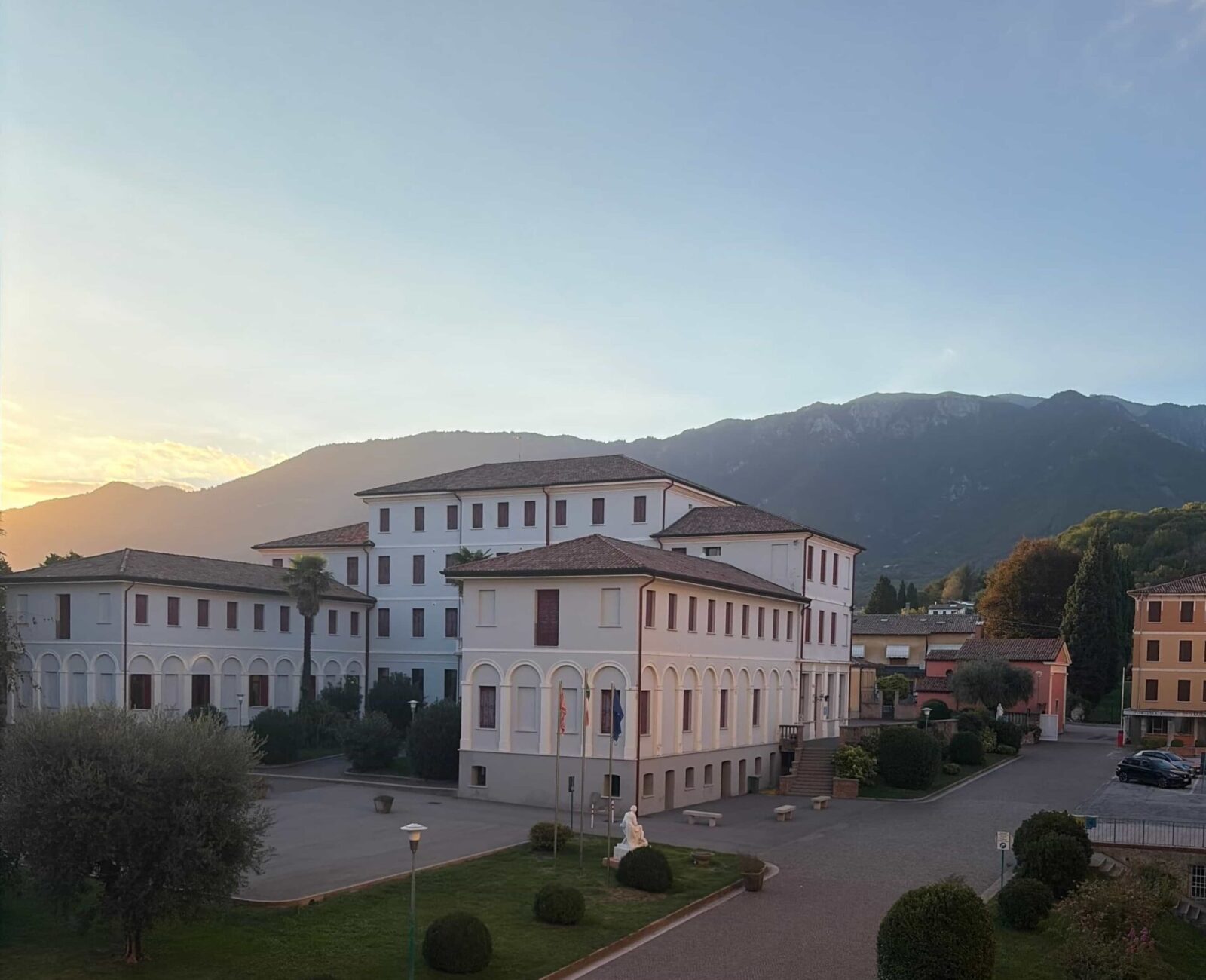 A hazy sunrise rises over mountains in the background. In front of them lie white historic buildings.