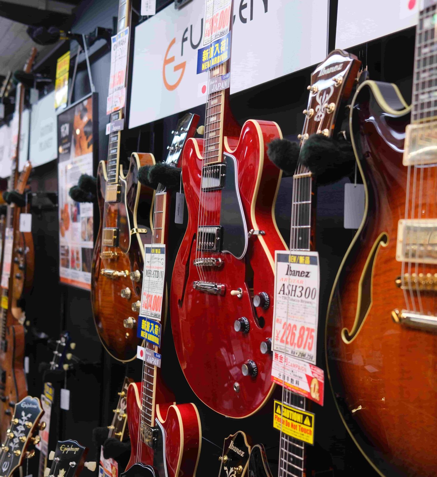 Red and orange guitars hang on a wall, displayed in a store.