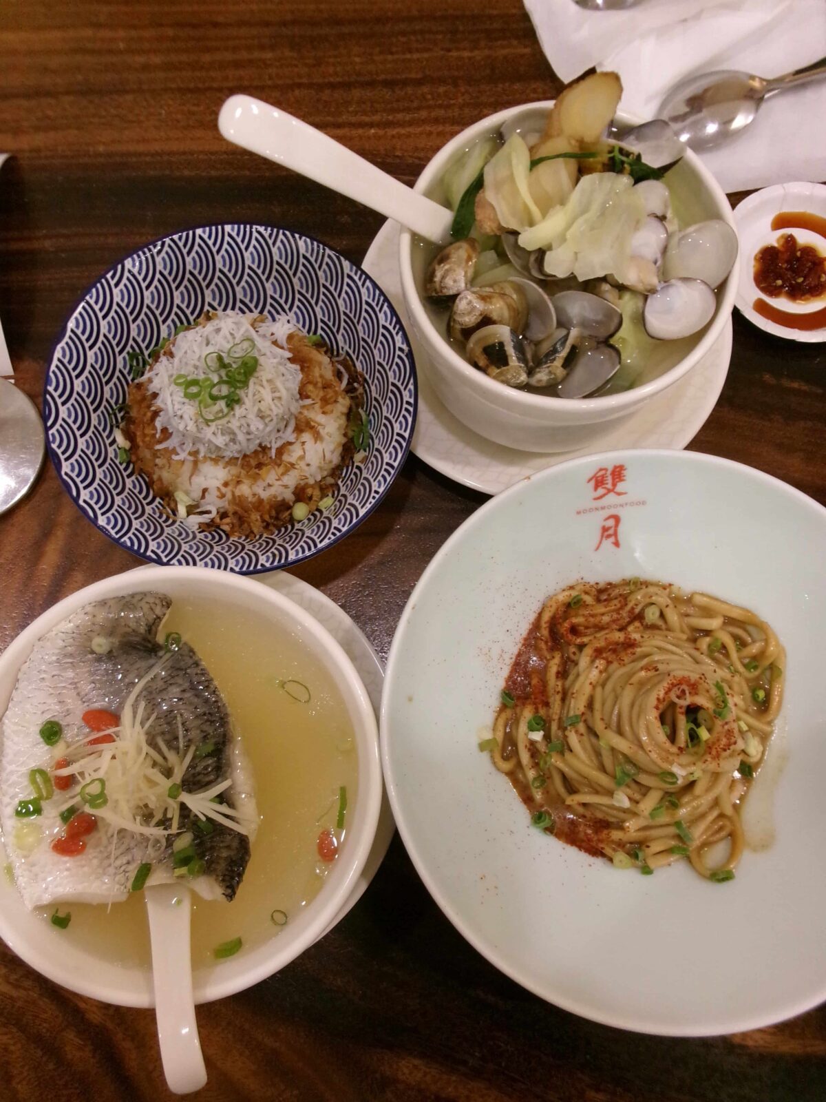 Four plates of food, one bowl of broth with fish; one bowl of rice, one bowl of noodles, one bowl with seafood.
