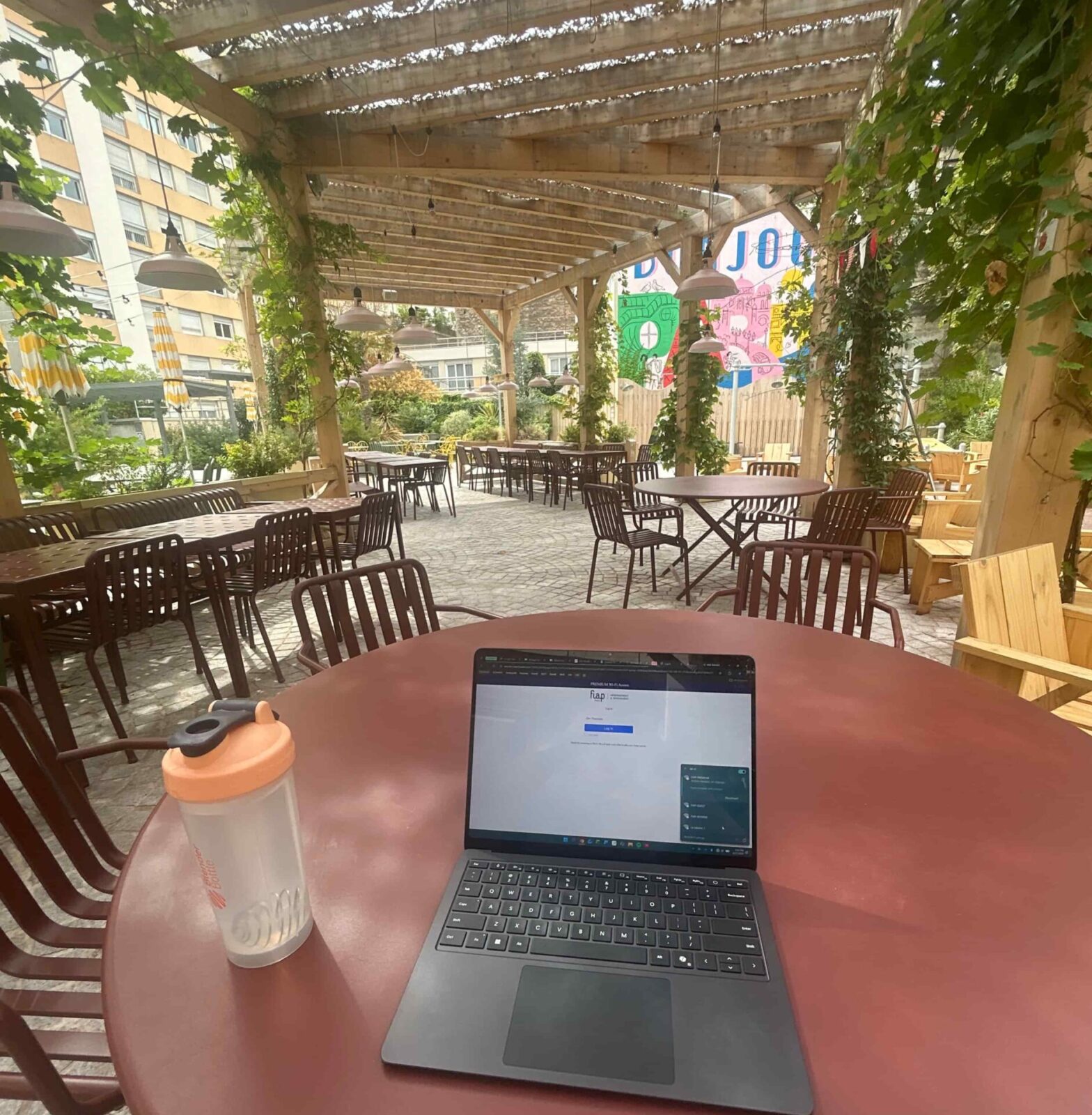 A laptop and water bottle sit on a red table in a cafe.